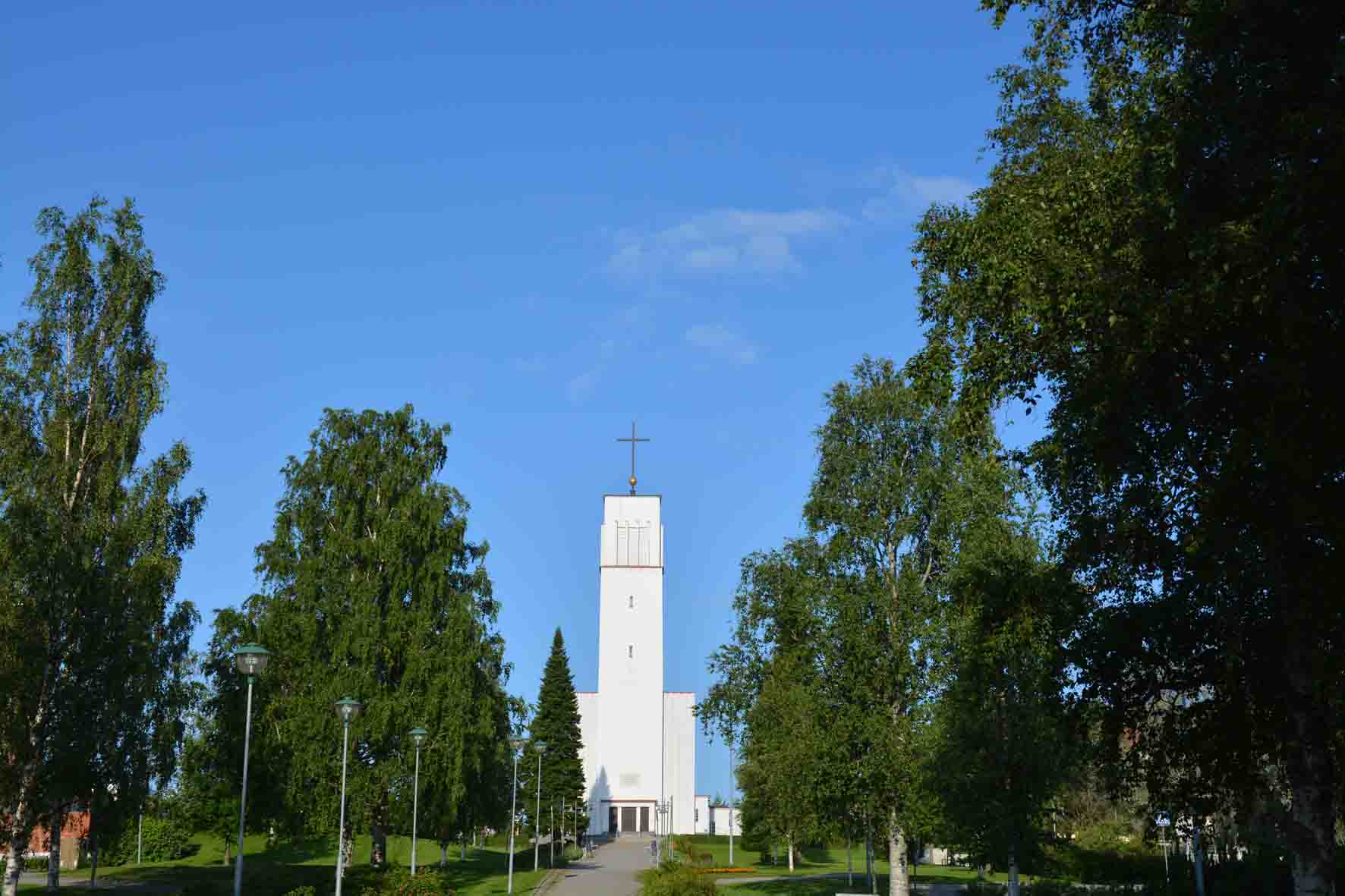 Valkea kirkkorakennus koivukujan päässä mäellä Iisalmessa.
