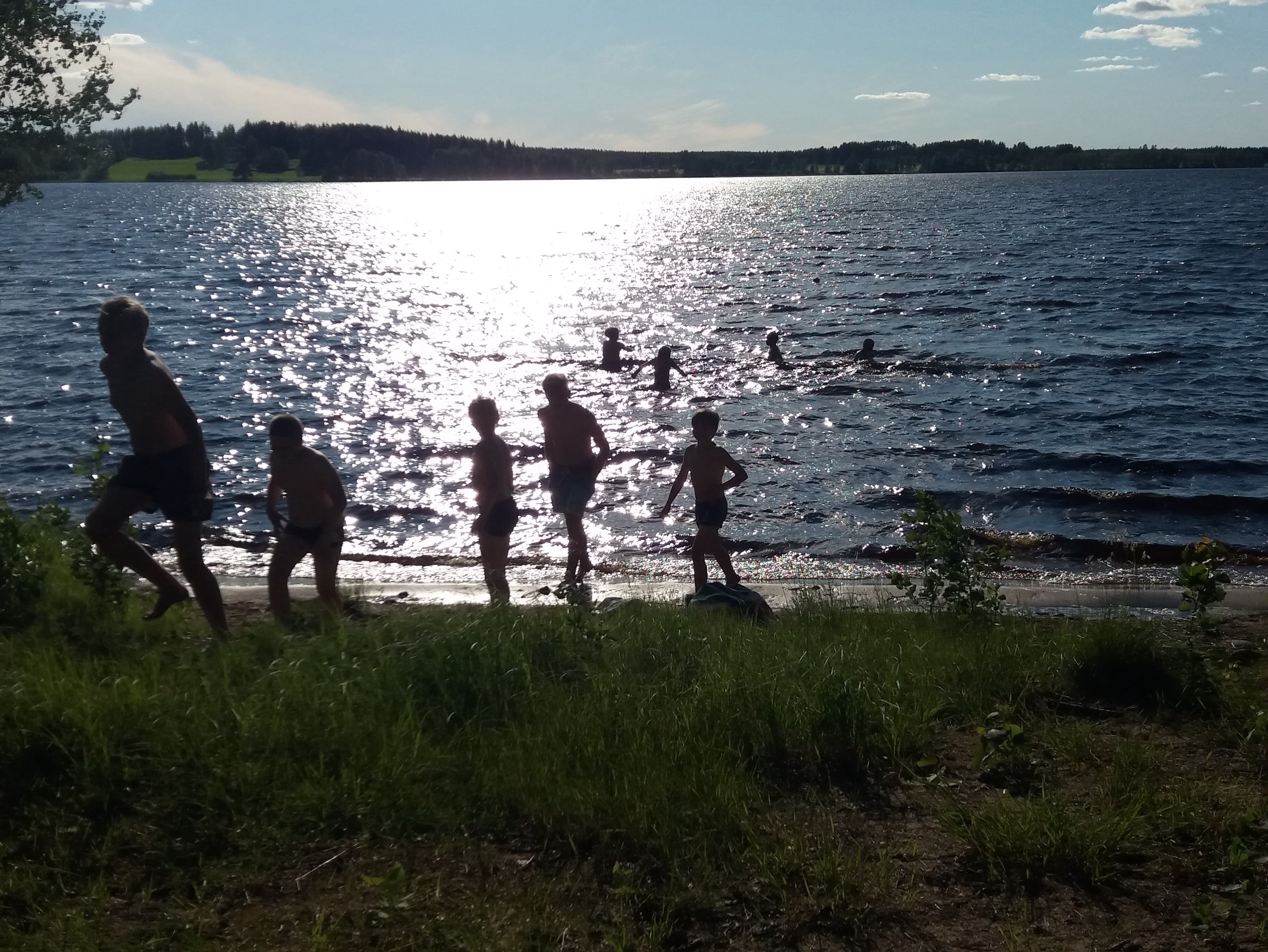 Lapsi menossa uimaan, aurinko kimmelää järven pinnasta.