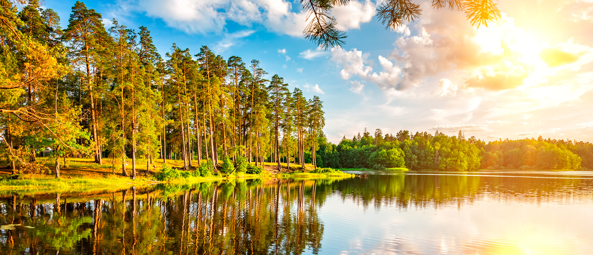 Kesäinen järvimaisema, aurinko paistaa pilven takaa.