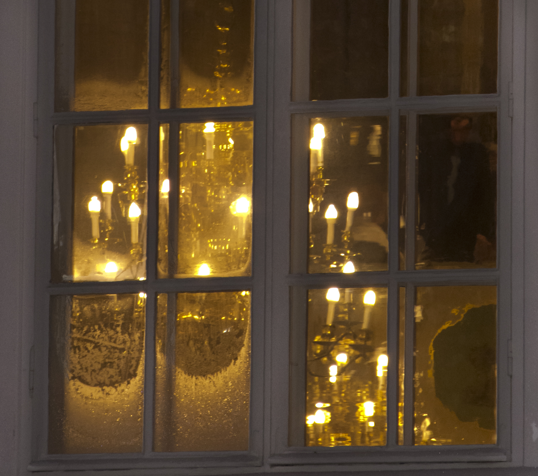 Ikkunan takana näkyy joulukuusi, jossa kynttilöitä.
